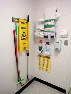 there is a yellow caution sign hanging on the wall next to cleaning supplies and brooms