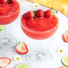 two margaritas with strawberries and lime garnish sit on a marble table