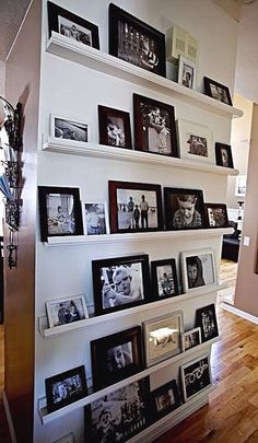 a wall filled with lots of pictures and framed photos next to a wooden floor in a living room