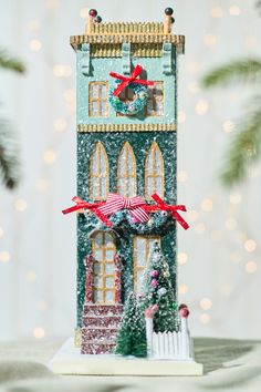 a christmas scene with a green building and red ribbon on the front, surrounded by pine branches