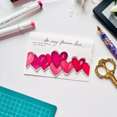 there is a card with hearts on it next to a pair of scissors and some pens