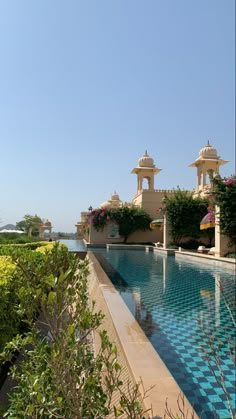 an outdoor swimming pool surrounded by greenery and flowers on a clear blue sky day