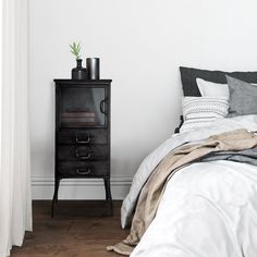 a bedroom with a bed, nightstand and plant on top of the night stand in front of the window