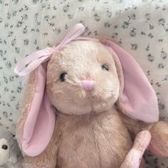 a stuffed rabbit sitting on top of a bed next to a small teddy bear with a pink bow