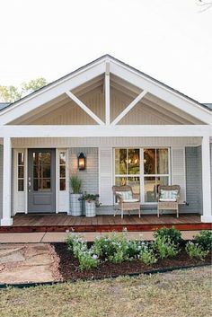 a blue house with white trim on the front porch and covered in plants, shrubs and trees