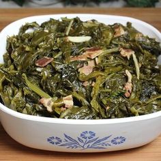 a white bowl filled with cooked greens on top of a wooden table next to a knife