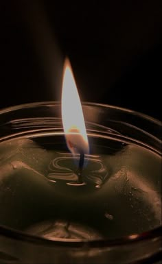 a lit candle in a glass bowl on a dark surface with only one light visible