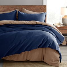 a bed with blue and brown comforters in a room next to a lamp on a table