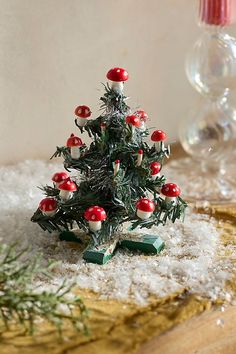 a small christmas tree with red and white mushrooms on it's top sitting in the snow