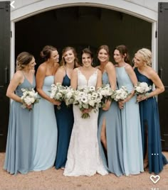 a group of women standing next to each other in front of a barn door holding bouquets