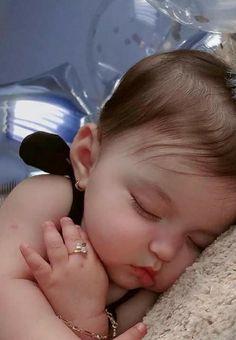 a baby sleeping on top of a blanket next to a teddy bear wearing a tiara