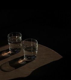 two glasses sitting on top of a wooden table next to each other in the dark