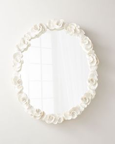 a round mirror with white flowers on the side and a wall in the back ground