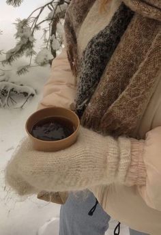 a woman holding a cup of coffee in her hand while standing on snow covered ground