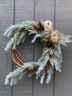 a wreath with pine cones, evergreen branches and small kittens on top is hanging from the side of a wooden wall