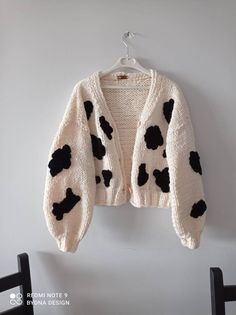 a white sweater with black spots on it hanging from a hanger next to a chair