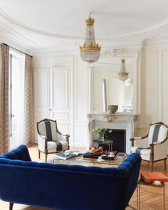 a living room filled with furniture and a chandelier hanging from the ceiling over a fire place