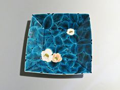 a blue plate with flowers on it sitting on a white table top next to a gray wall