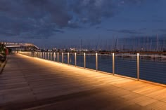 a long wooden pier with boats in the background at night, lit up by lights