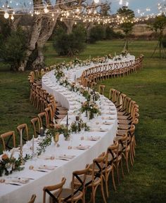 a long table is set up with white linens and greenery for an outdoor dinner