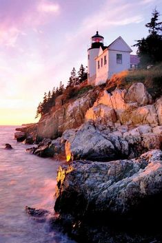 a light house sitting on top of a rocky cliff next to the ocean at sunset