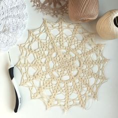 crocheted doily, yarn and scissors on a white surface with two balls of thread