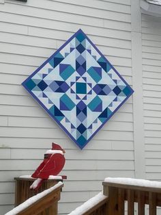 a blue and white quilt hanging on the side of a house next to a red bird