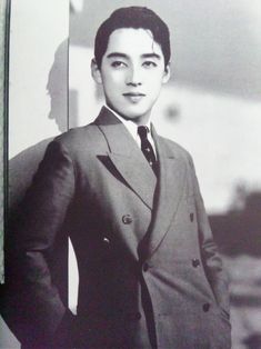 an old photo of a man in a suit and tie standing next to a wall