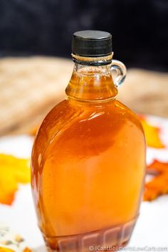 a glass bottle filled with liquid sitting on top of a white table covered in leaves