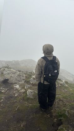 a person standing on top of a rocky hill in the rain with a back pack