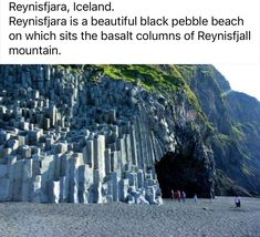 people are walking on the beach in front of a large formation of rocks that look like mountains