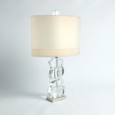 a clear glass table lamp with a white shade on the base and a beige drum light