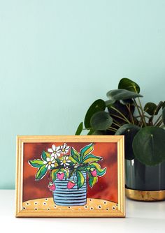 a potted plant sitting on top of a white table next to a framed painting