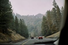 two cars driving down the road in front of some trees and hills on a foggy day