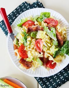 a white plate topped with pasta salad next to a bowl of carrots and ketchup