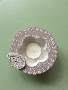 a small white candle sitting in a paper plate on a green tableclothed surface