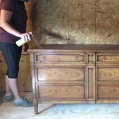 a woman spray painting a wooden dresser in a room with wood paneling and plywood walls