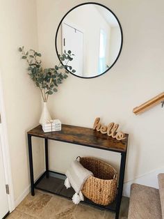 a mirror on the wall above a wooden table with a basket underneath it and a vase filled with flowers