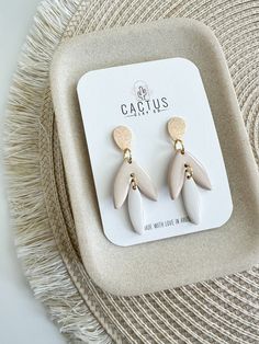 a pair of white and gold earrings sitting on top of a table next to a straw hat