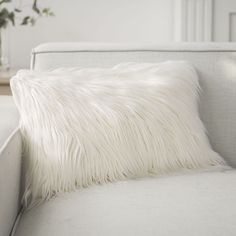 a white couch with a fluffy pillow on it's back and a plant in the background