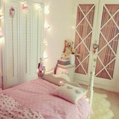 a bedroom decorated in pink and white with fairy lights on the wall above the bed