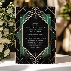 a black and green art deco wedding card on a table with white flowers in the background