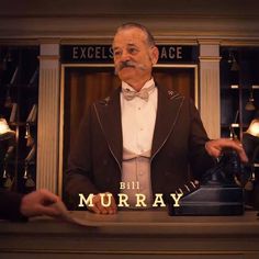 a man in a tuxedo standing behind a counter