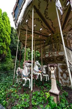 an old fashioned merry go round in the middle of some trees and bushes with statues on it