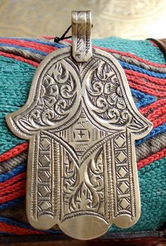 a silver hamsa hanging from a rope on top of a blue and red blanket