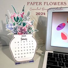 a laptop computer sitting on top of a desk next to a paper flower vase calendar