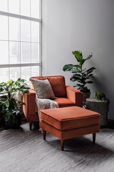 an orange chair and footstool in front of a window with potted plants