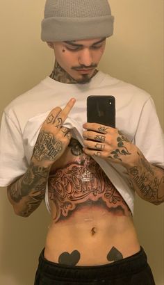 a man with tattoos on his stomach holding a cell phone and pointing at the screen