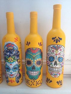 three yellow bottles with skulls painted on them are lined up against a white wall,