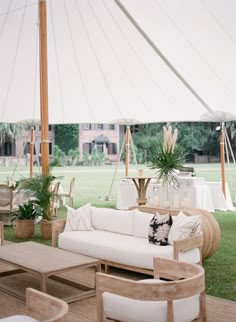 an outdoor area with couches, tables and chairs under a large white tent on the grass